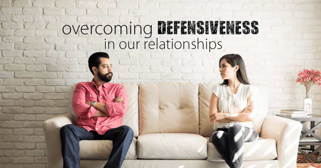 defensive couple on couch with arms crossed and the words "overcoming defensiveness in our relationships" in words above it